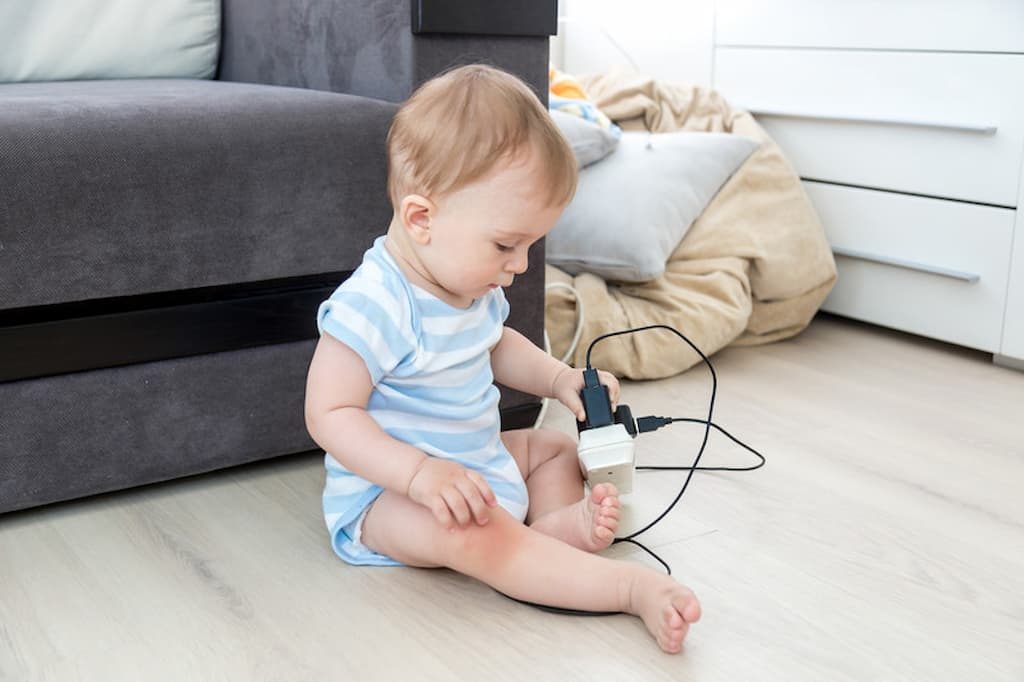 Baby sitting on the floor and playing with cords